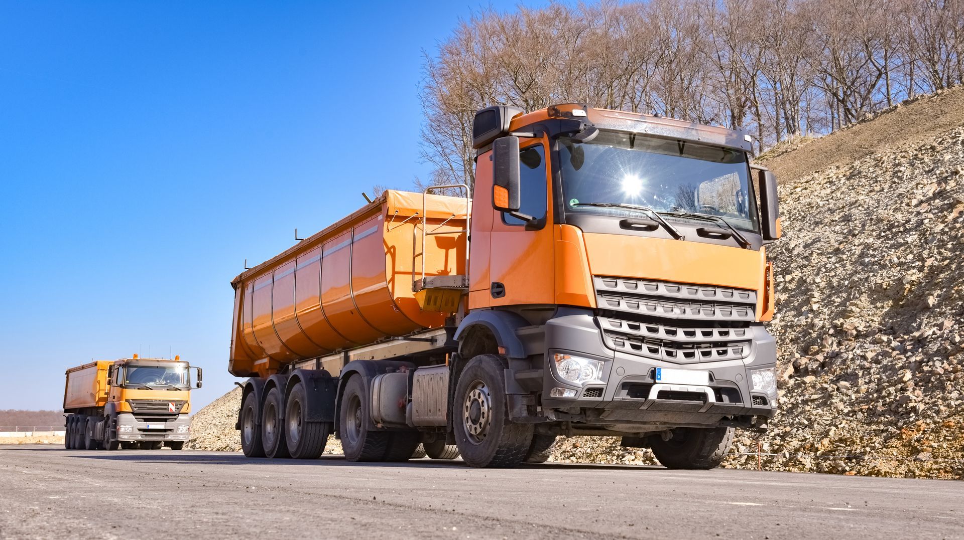 Deux camions à benne orange sur une route.