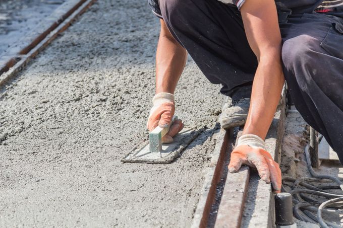 Personne lissant du béton humide avec une truelle sur un chantier de construction, portant des gants.