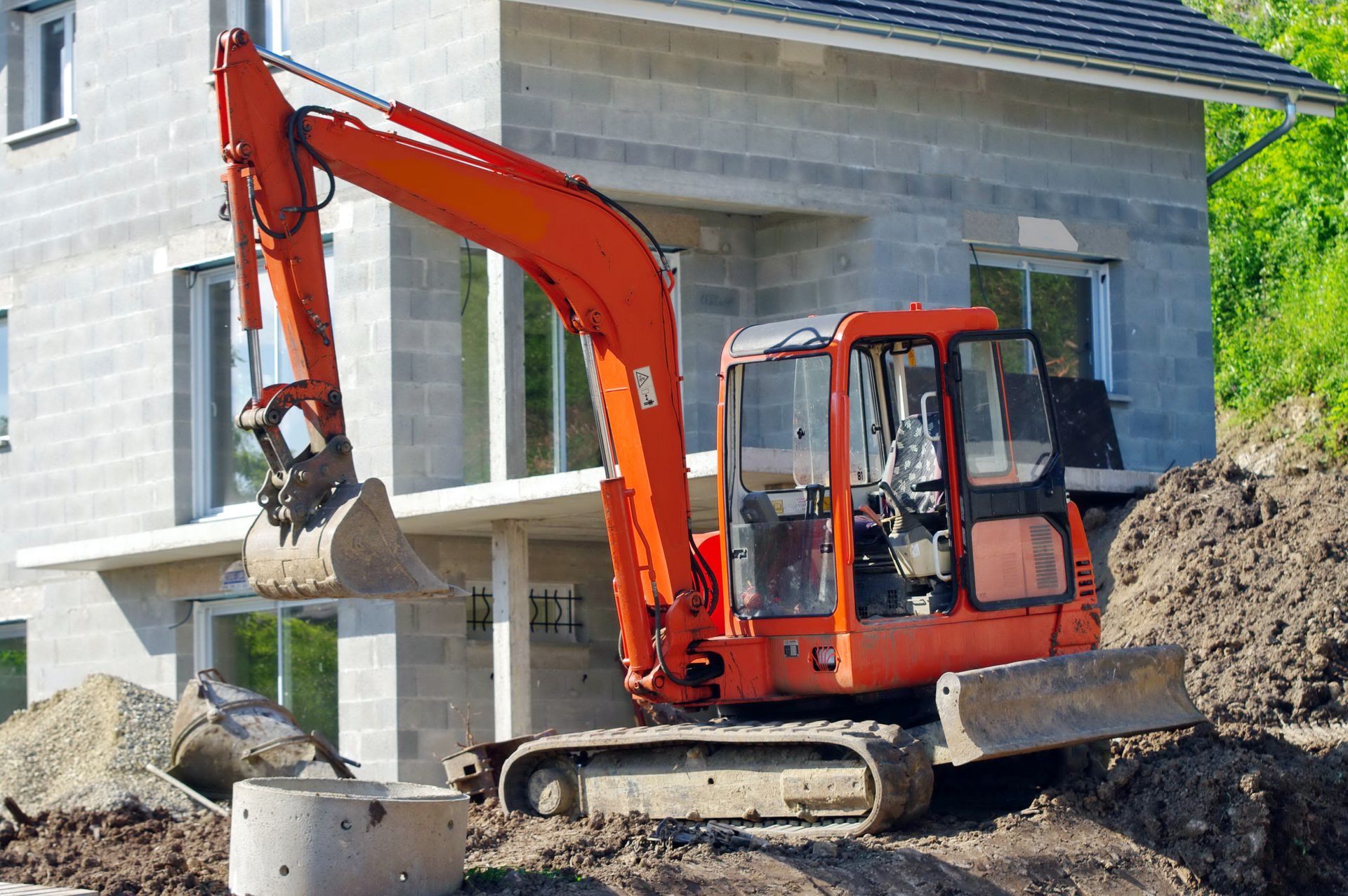 Excavatrice orange creusant près d'un bâtiment.