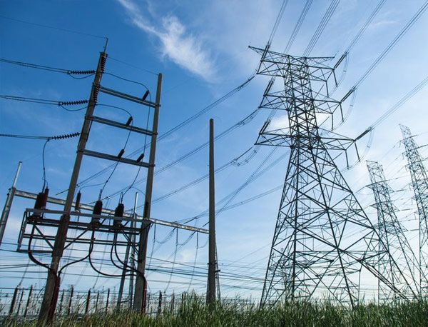 Una hilera de líneas eléctricas y torres en un campo con un cielo azul de fondo.