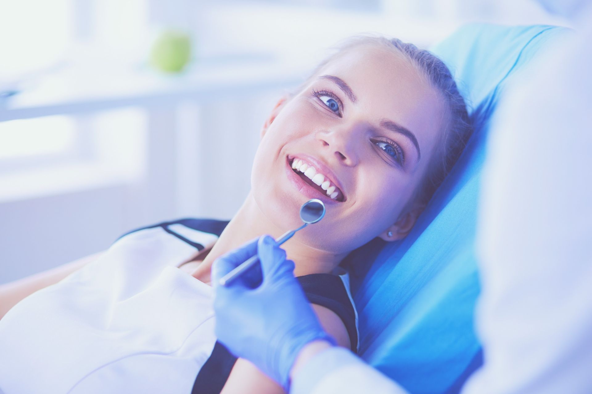 Una mujer sonríe mientras un dentista le examina los dientes.