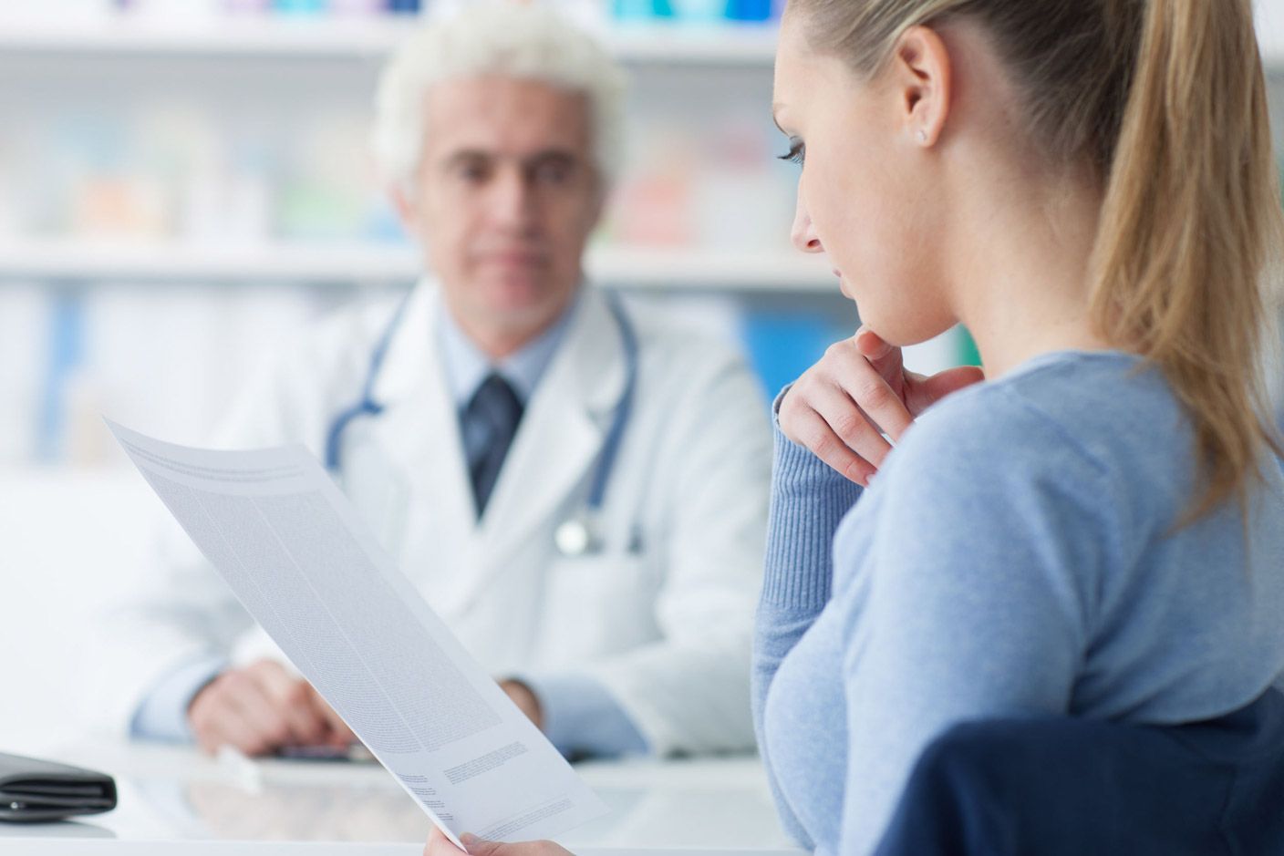 Una mujer está sentada frente a un médico mirando un trozo de papel.