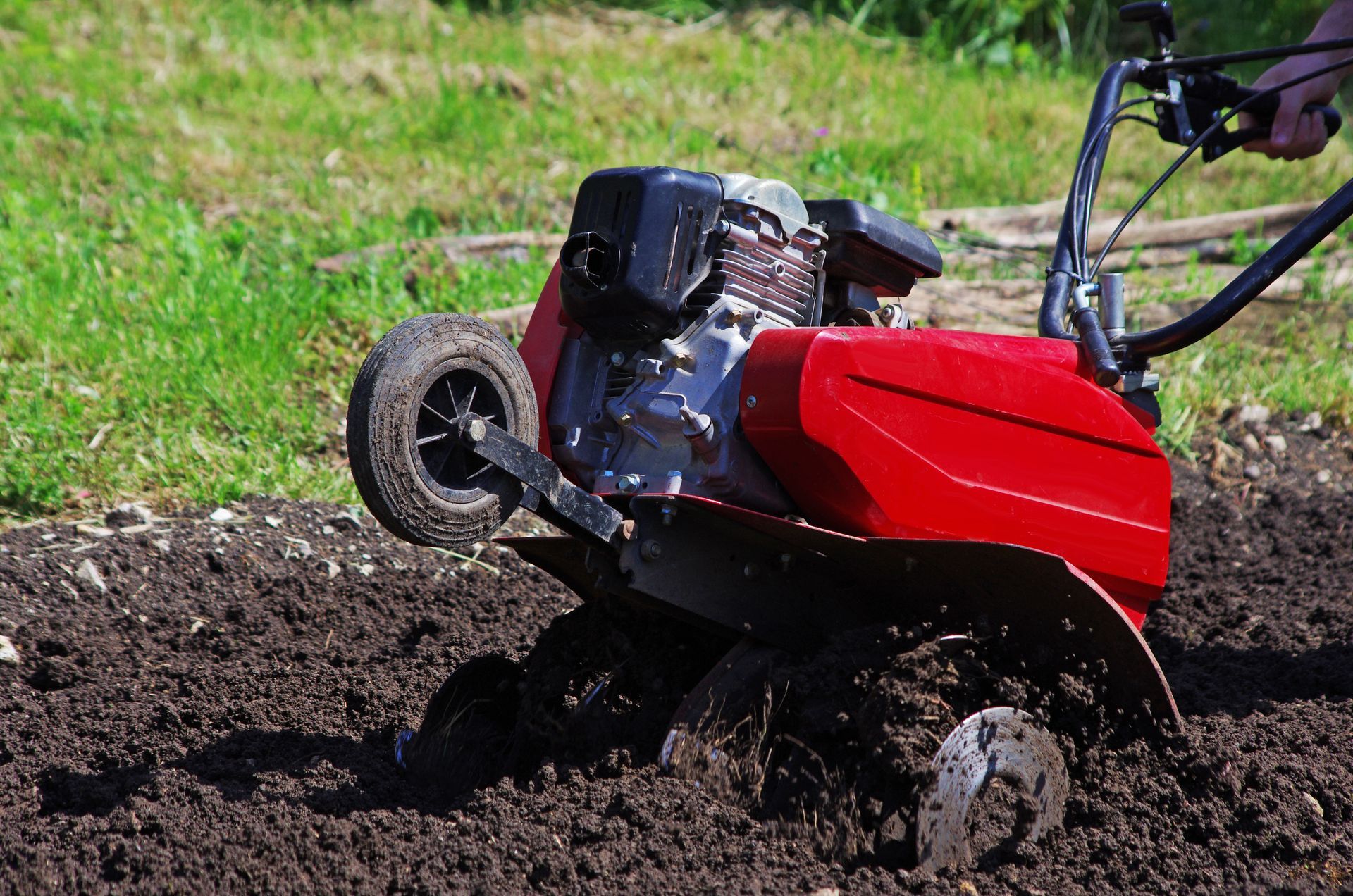 Motobineuse rouge creusant dans un sol sombre sur un terrain herbeux.