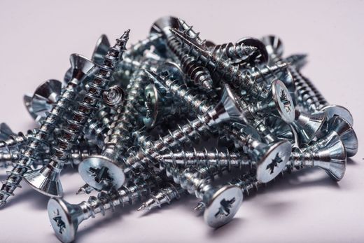 Pile de vis argentées brillantes sur une surface blanche.