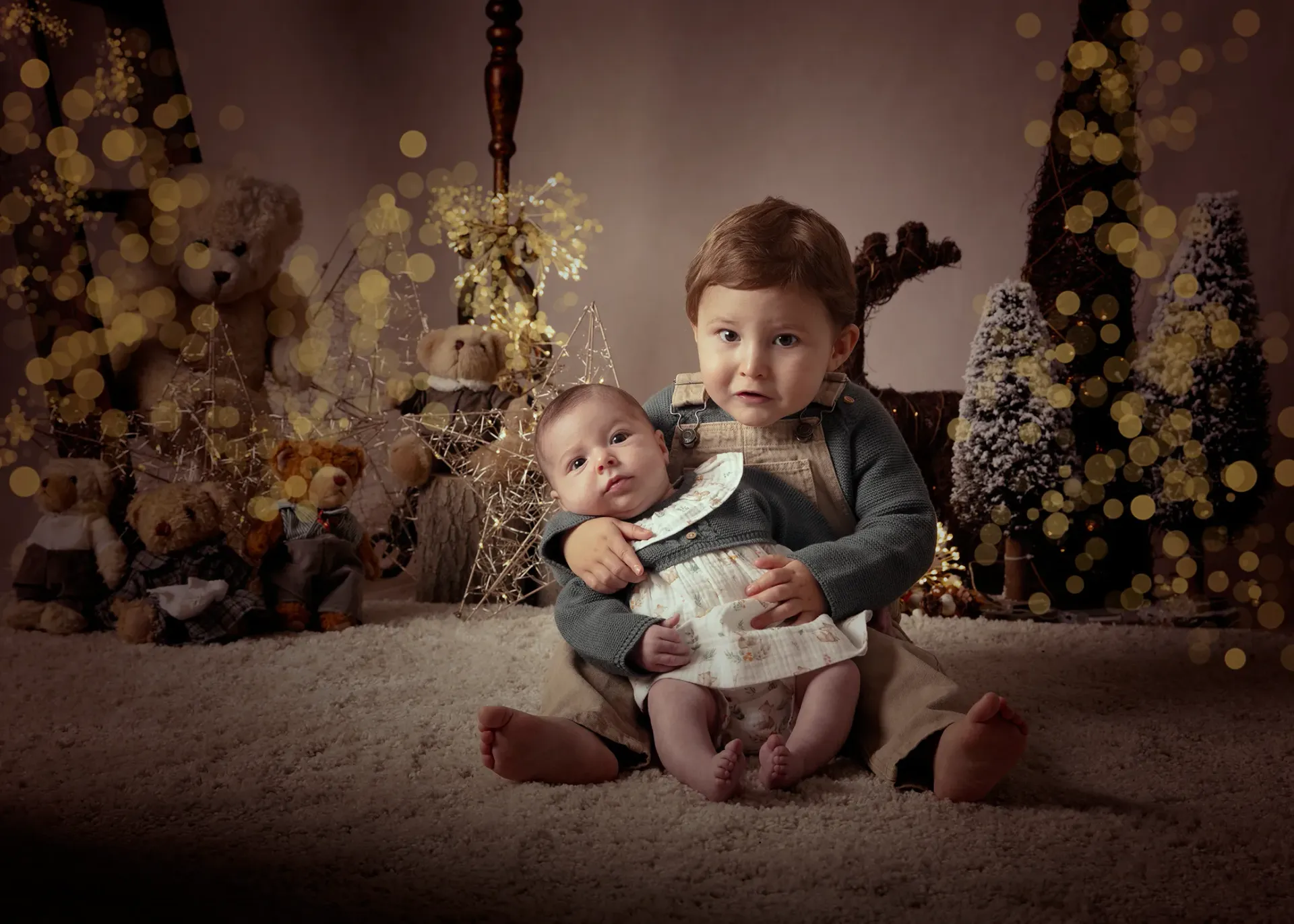 Niño sosteniendo a un bebé en un ambiente navideño con luces y decoraciones.