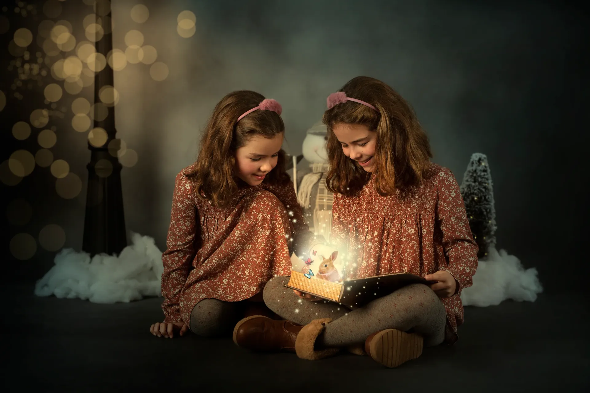 Dos chicas con el pelo rizado, sentadas y mirando una caja abierta y brillante en una escena oscura e invernal.