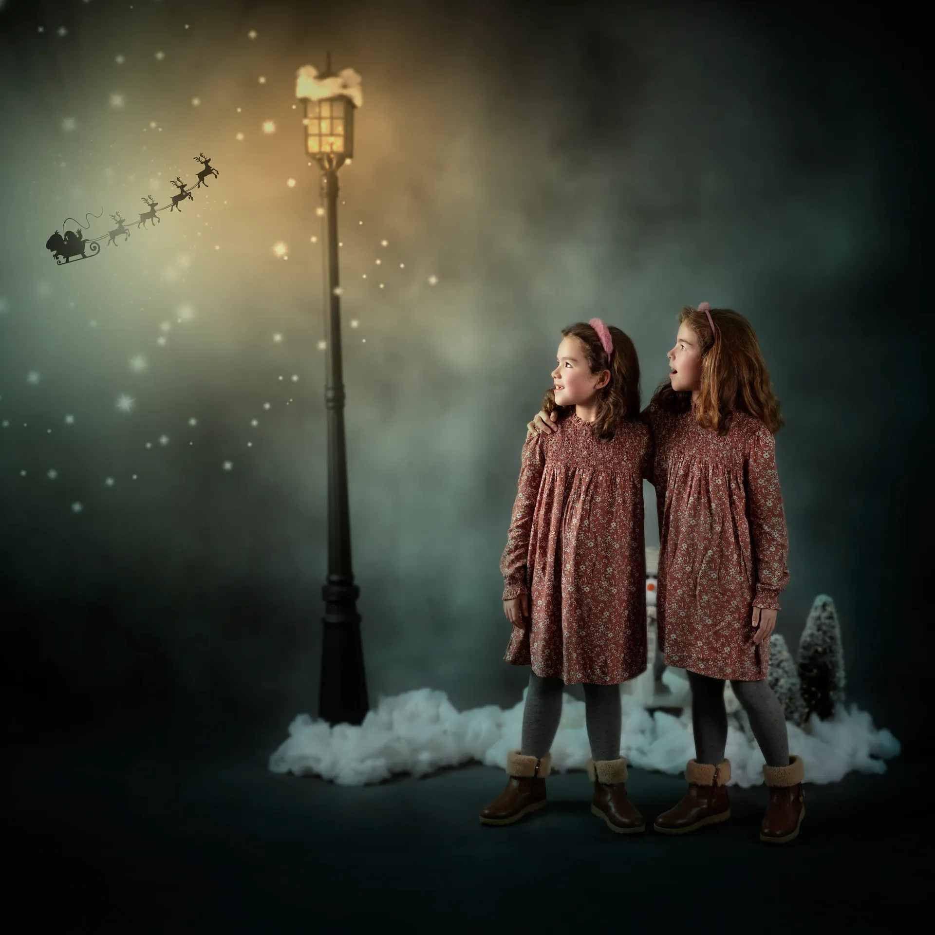 Dos niñas con vestidos miran hacia una farola y la silueta del trineo de Papá Noel, la nieve y un fondo oscuro.
