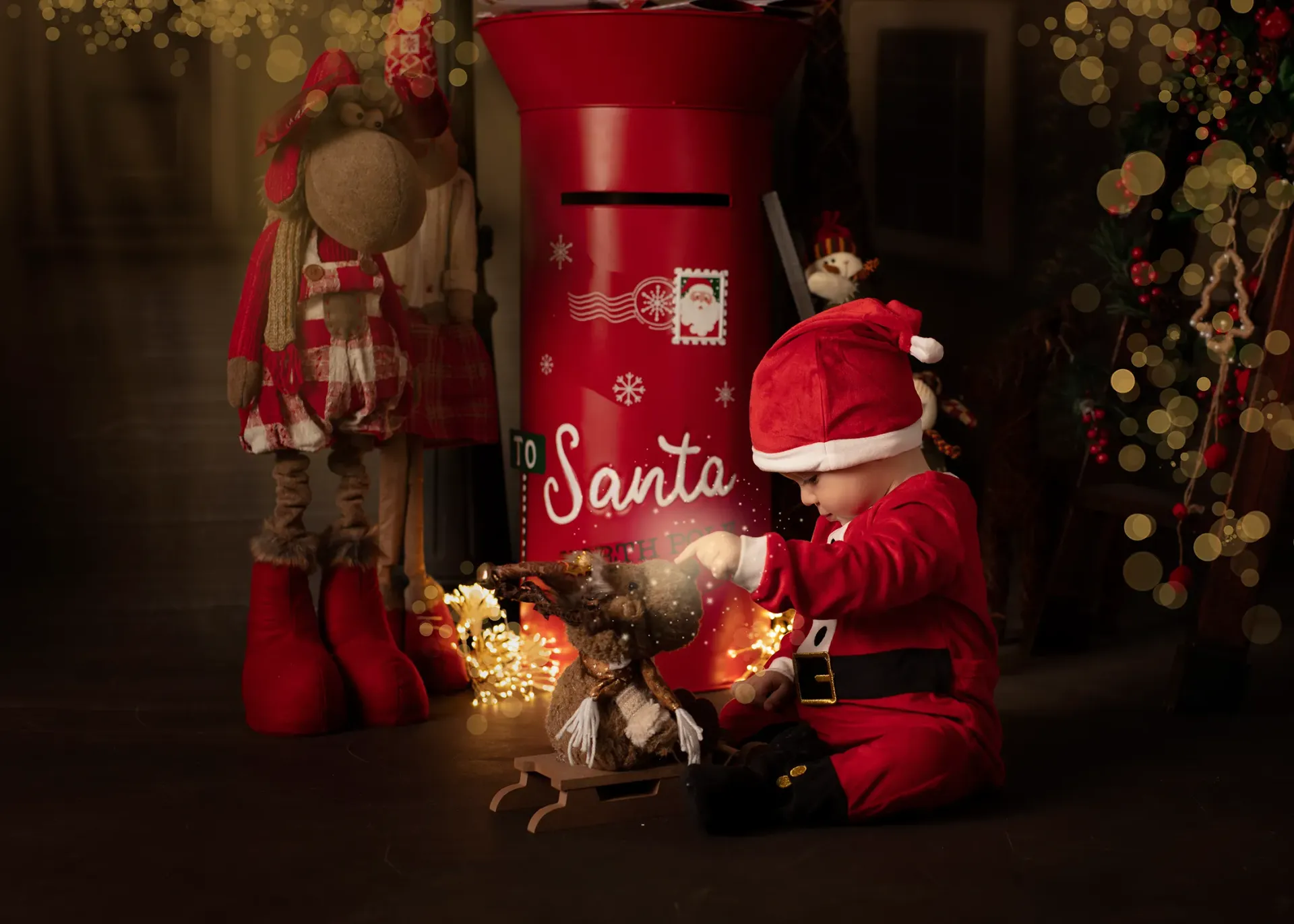 Niño vestido de Papá Noel con renos, luces navideñas y un buzón rojo.