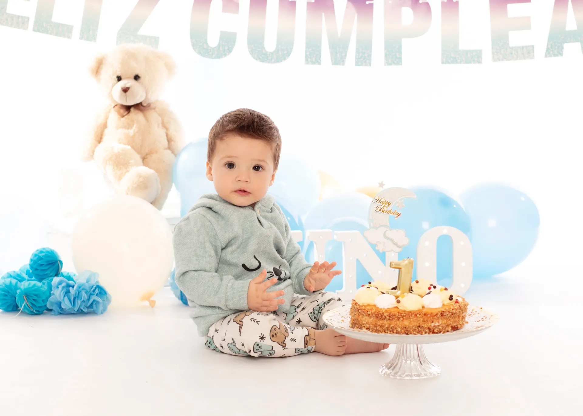 El bebé se sienta cerca del pastel, los globos y las letras del juego 