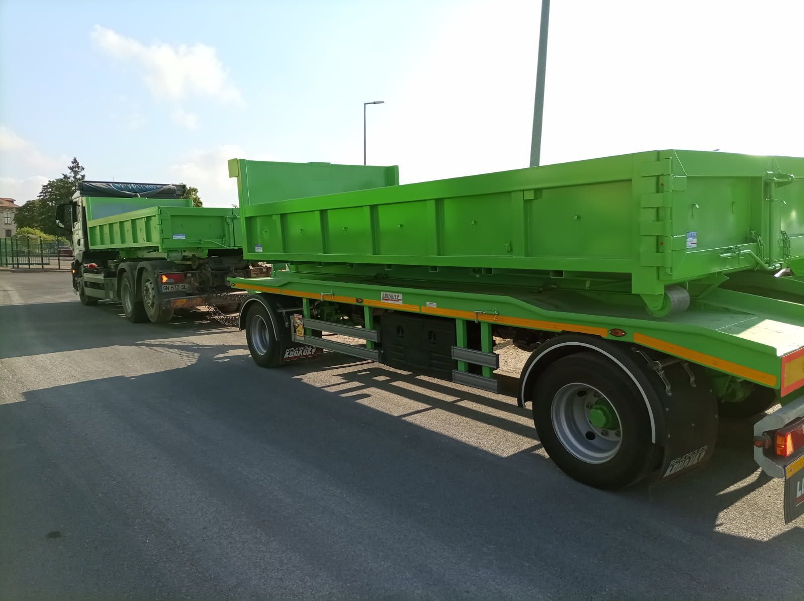 Des camions-bennes verts sur une route, l'un tirant une remorque avec un autre camion-benne vert.