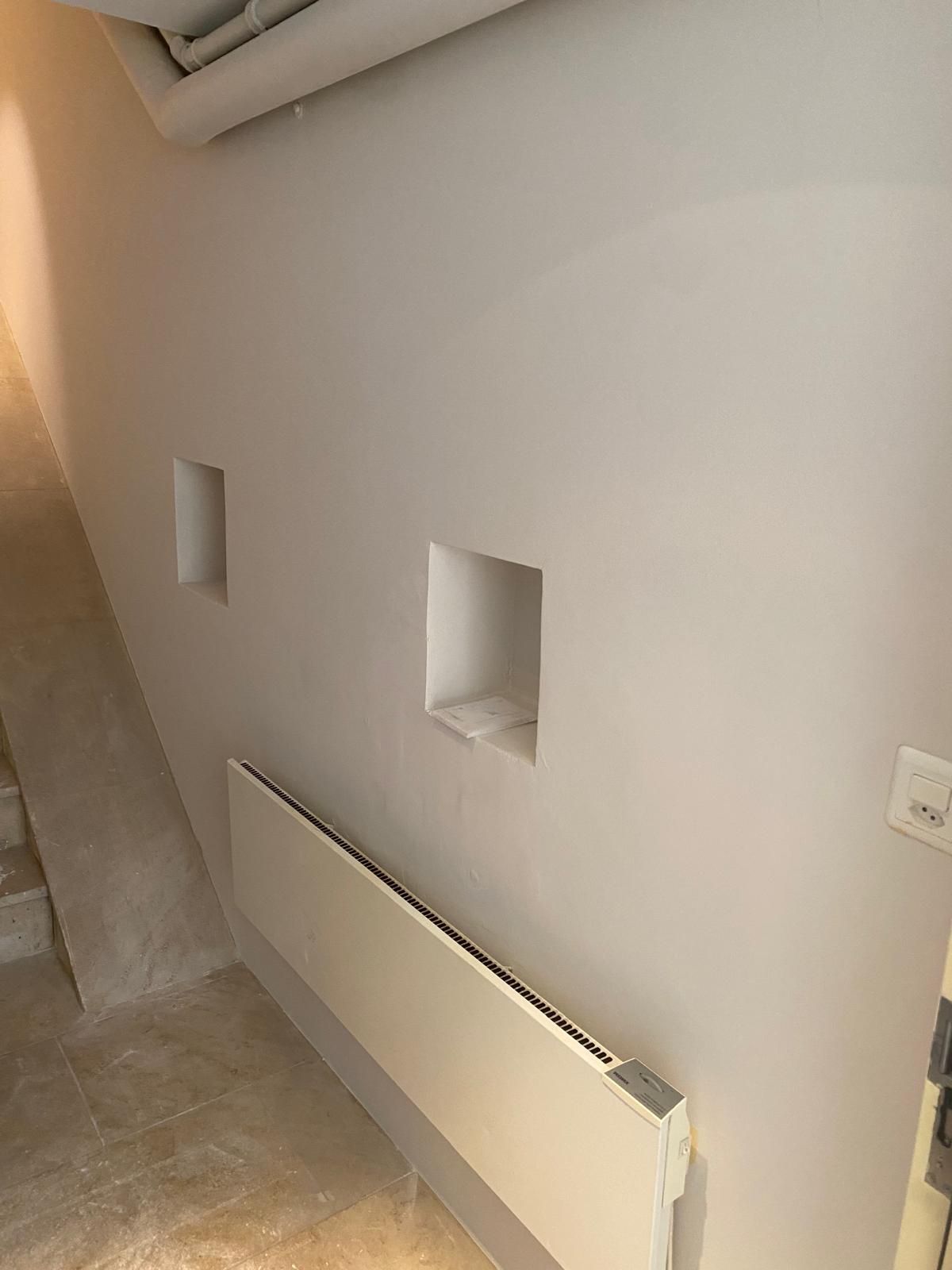 Eine kunstvoll verzierte Decke mit Kronleuchter, helle Wände und gelbe Vorhänge, die durch die Fenster sichtbar sind.