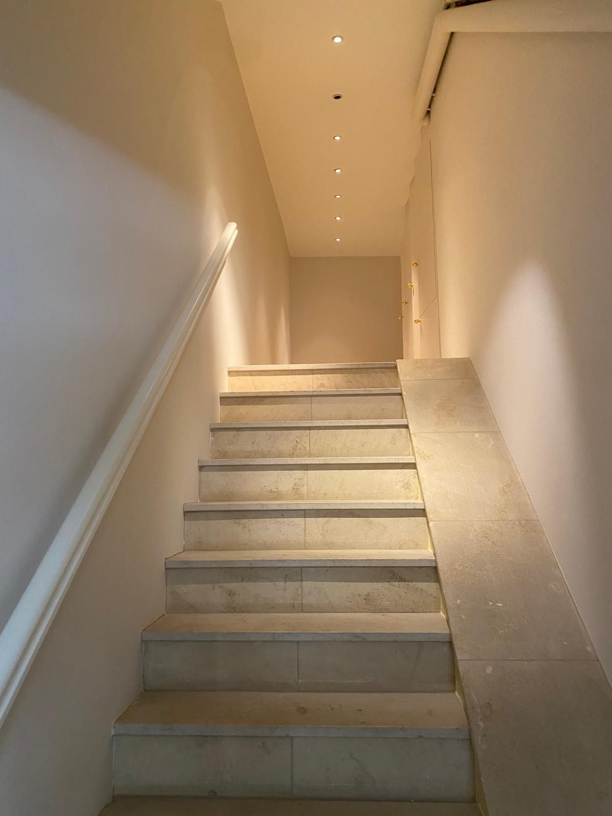 Zwei weisse, moderne Lampen, die nach unten geneigt sind, eine auf einem Tisch, vor einer orangefarbenen Wand.