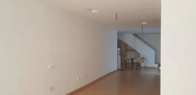 Habitación vacía, de paredes blancas y suelo de madera. Al fondo, una escalera sube.
