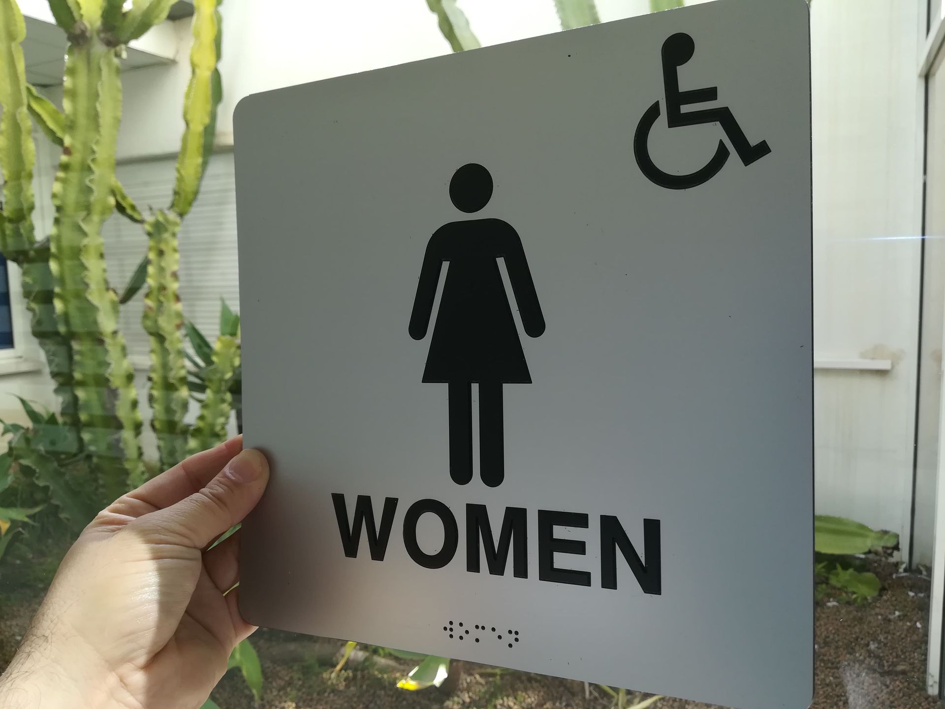 Una persona sostiene un cartel que indica un baño de mujeres.