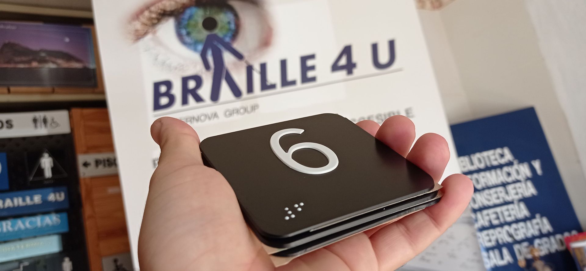 Una persona sostiene un cartel en braille 4 u en su mano.