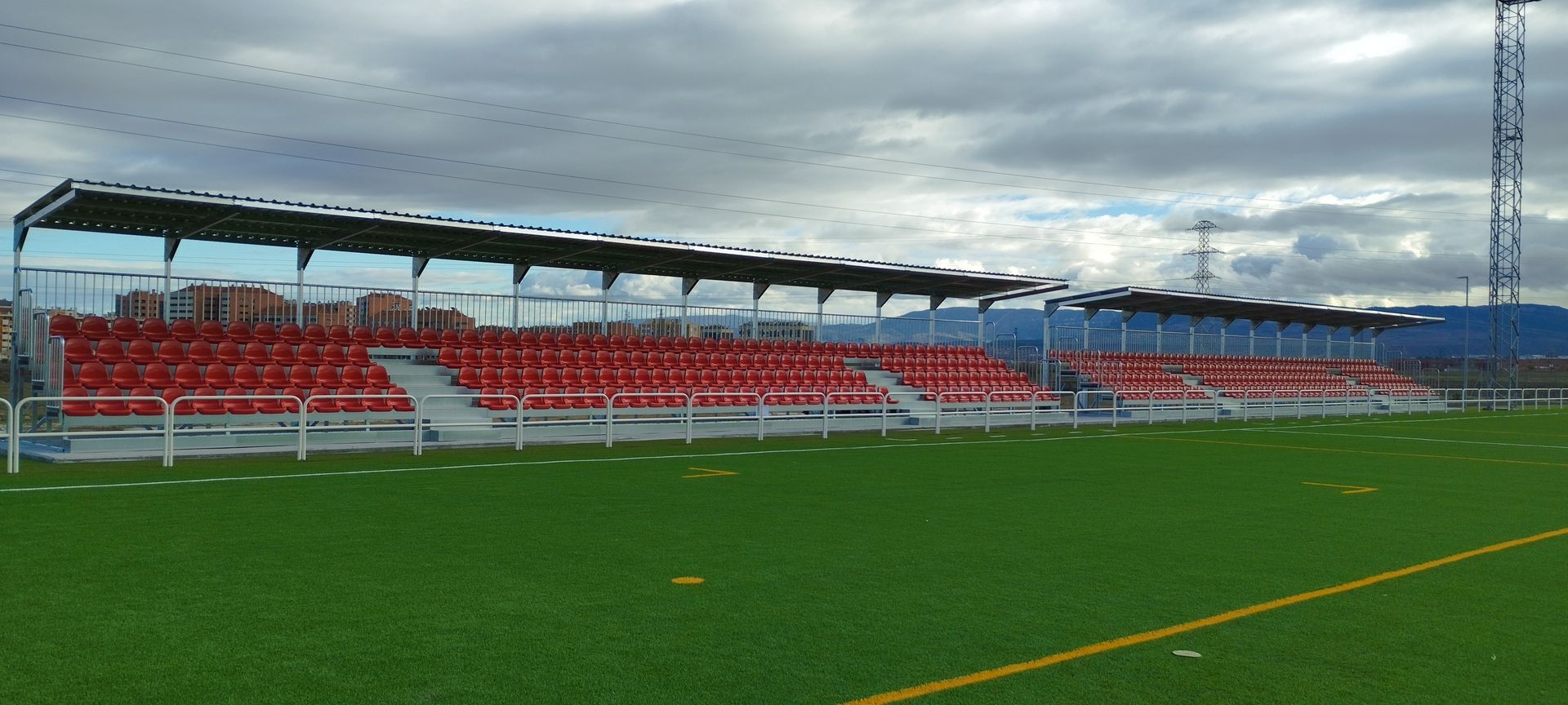 Un campo de fútbol con asientos rojos y un estadio al fondo.