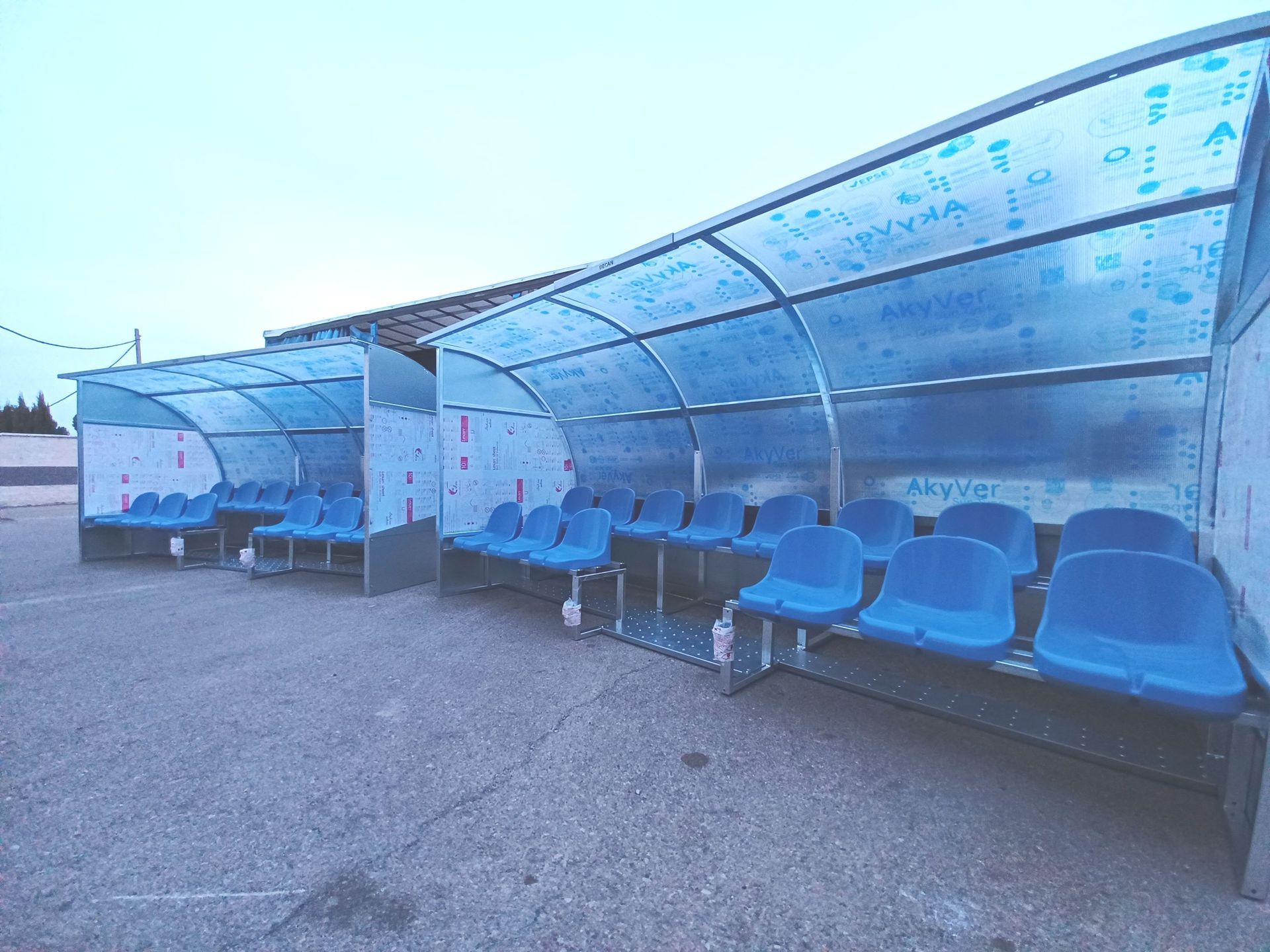Una fila de sillas azules bajo un techo transparente en un estacionamiento.