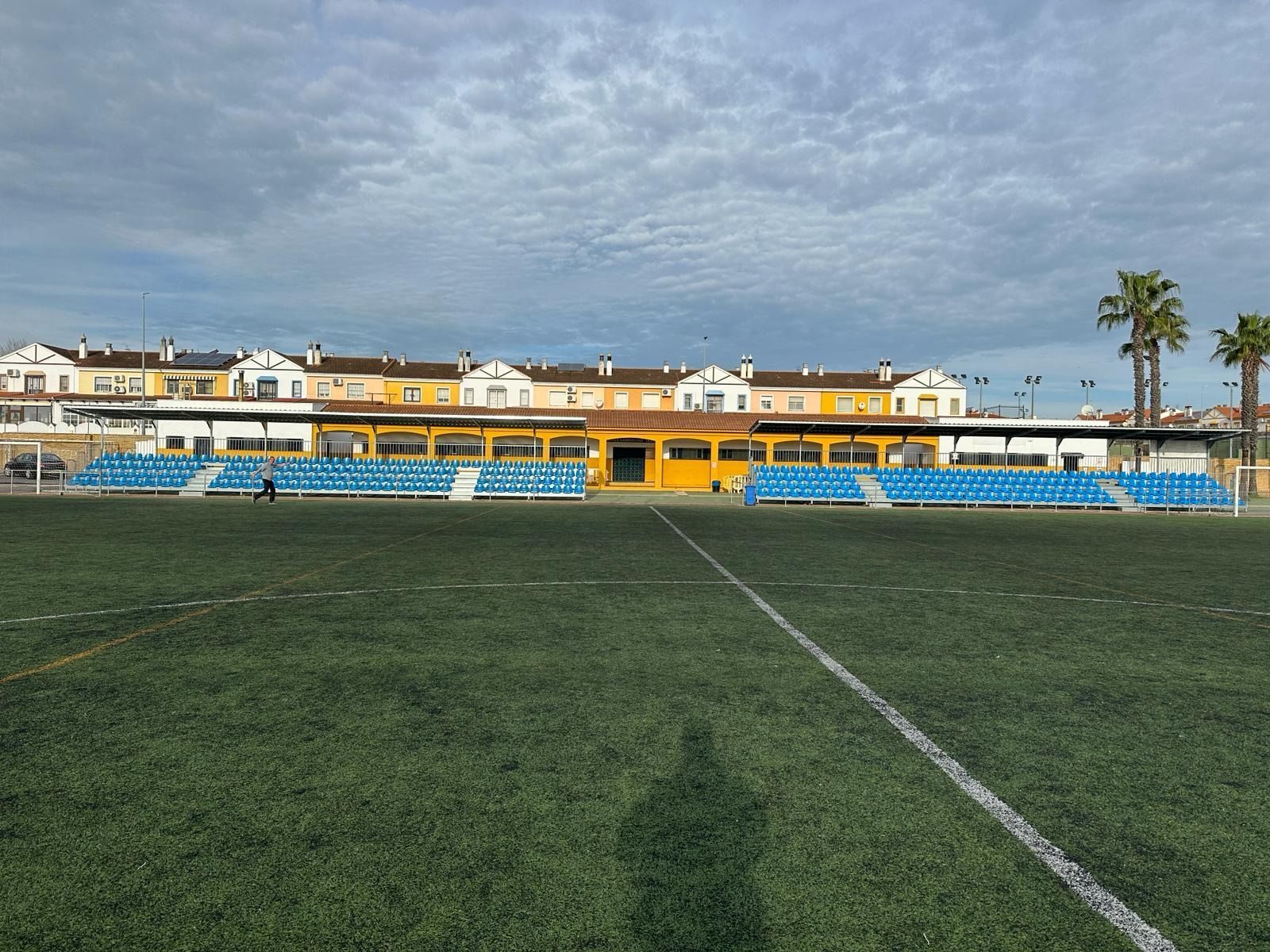 Un campo de fútbol con asientos azules y un edificio amarillo al fondo.