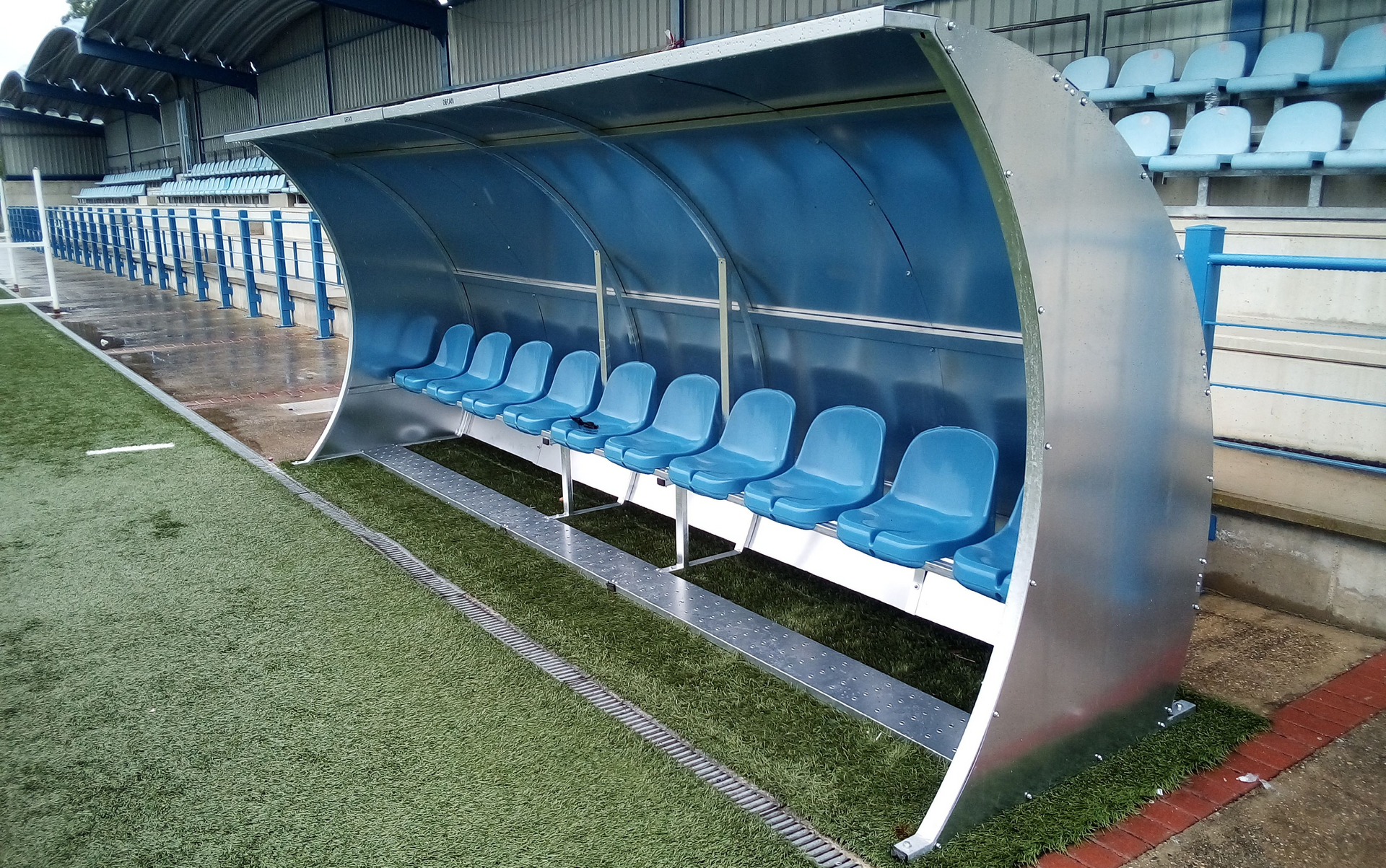Un refugio de metal con asientos azules en un campo de fútbol.