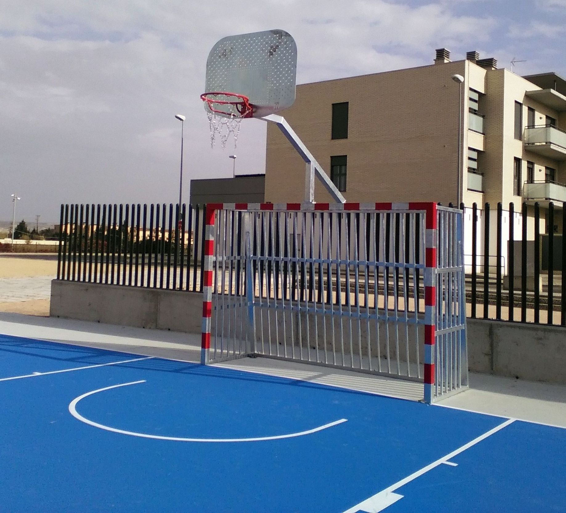 Una cancha de baloncesto azul con una valla y un edificio al fondo.
