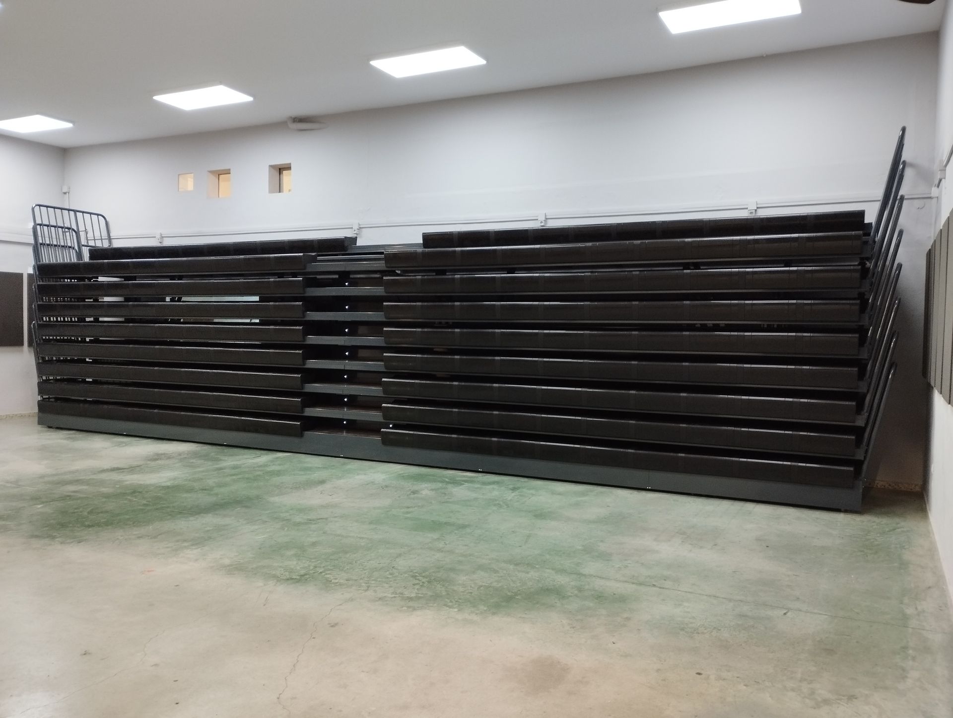 Una gran sala vacía con una fila de gradas negras.