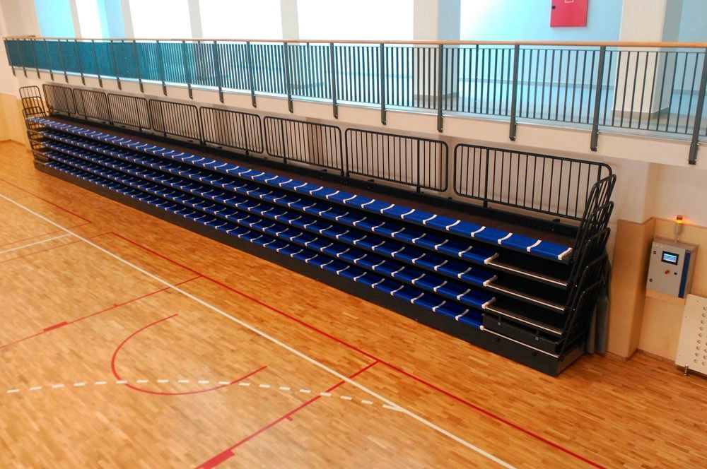 Una fila de asientos azules sobre un piso de madera en una cancha de baloncesto.