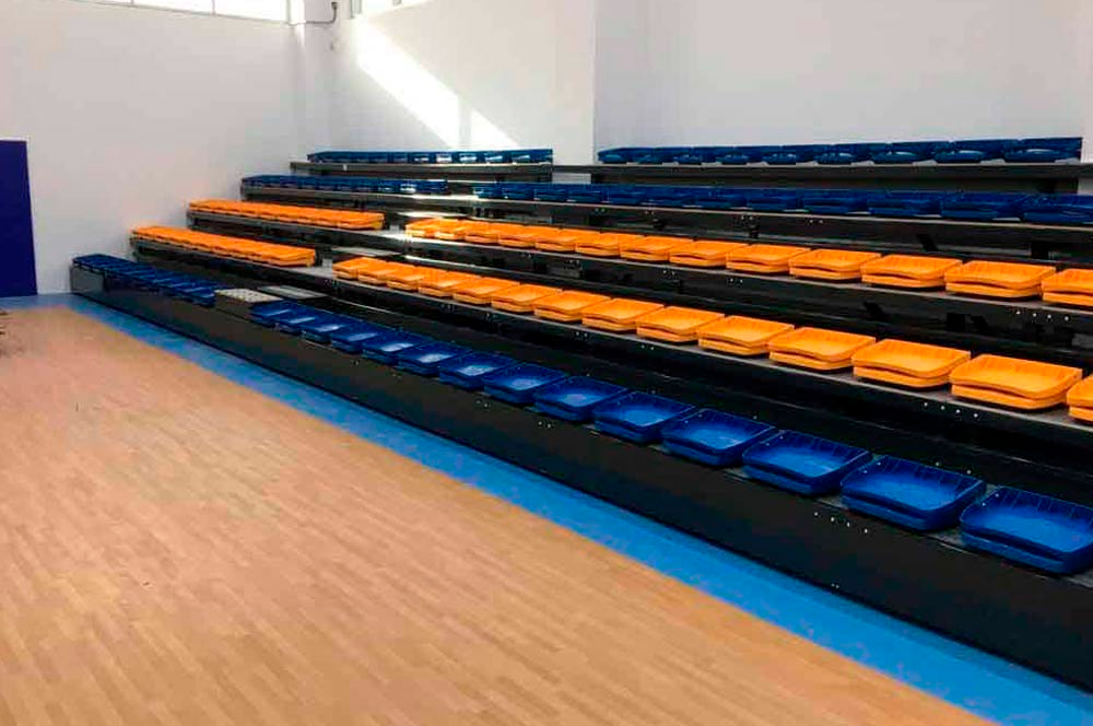 Una fila de asientos azules y naranjas en un estadio con piso de madera.