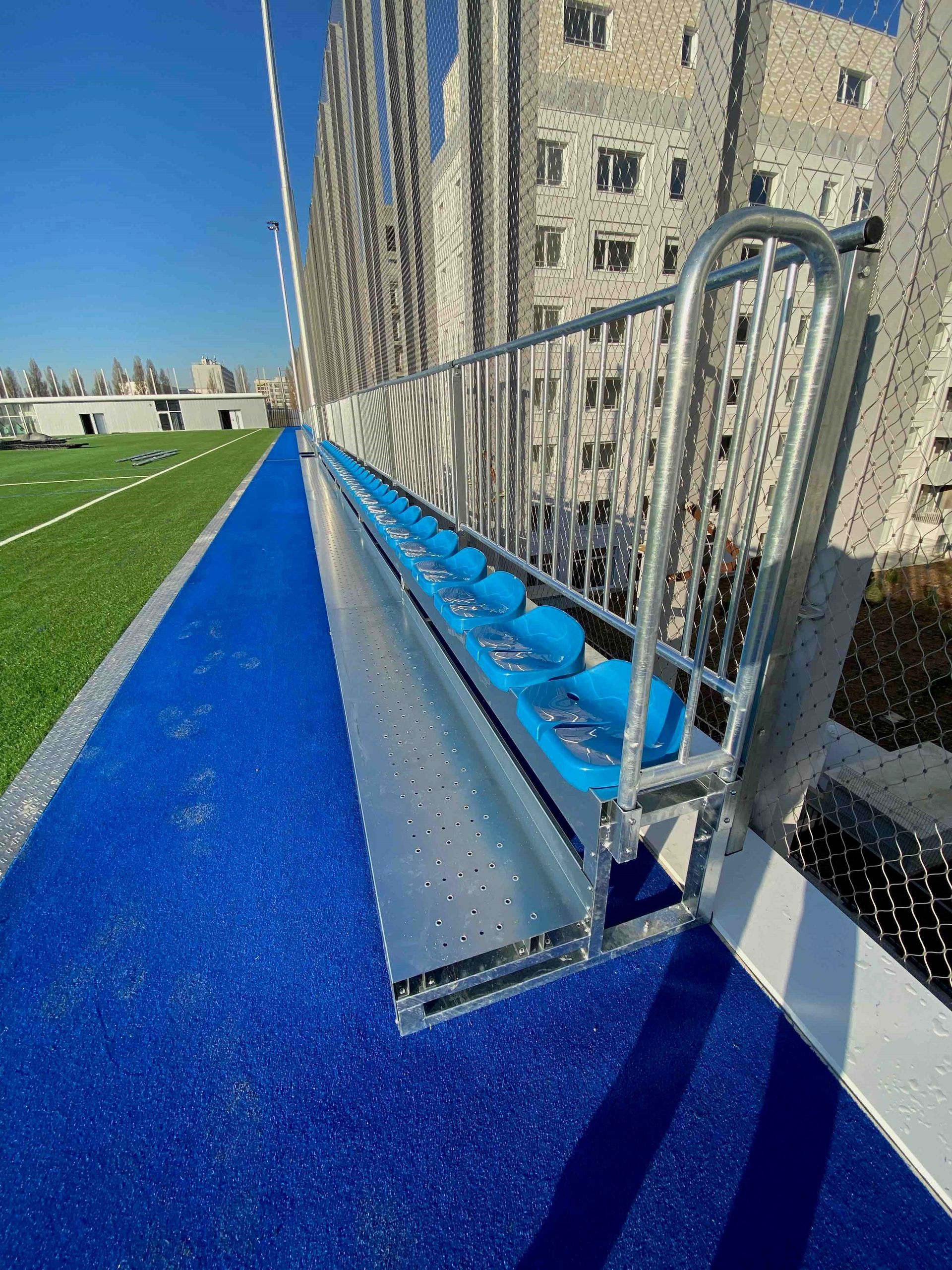 Una fila de asientos azules en un campo de fútbol al lado de una valla.