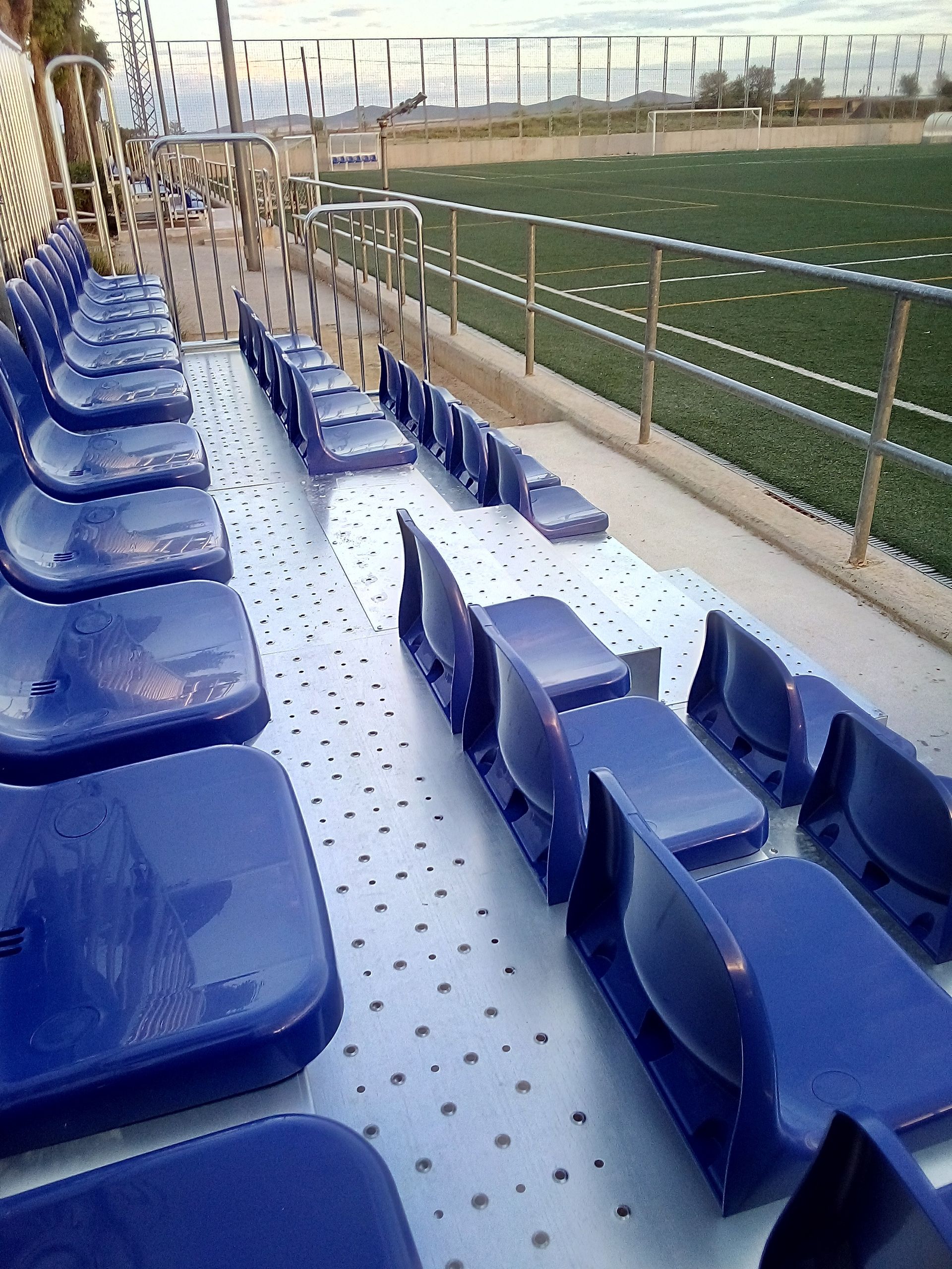 Una fila de asientos azules en un estadio con un campo al fondo.