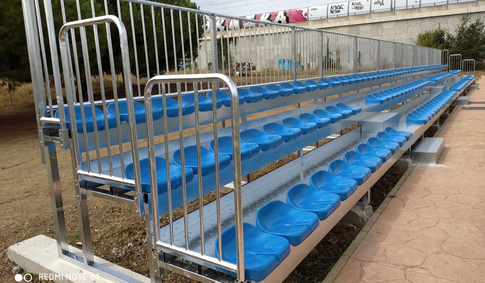 Una fila de gradas de plástico azul con una barandilla de metal.