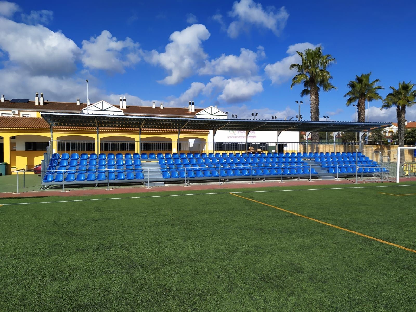 Un campo de fútbol con asientos azules y un edificio al fondo.