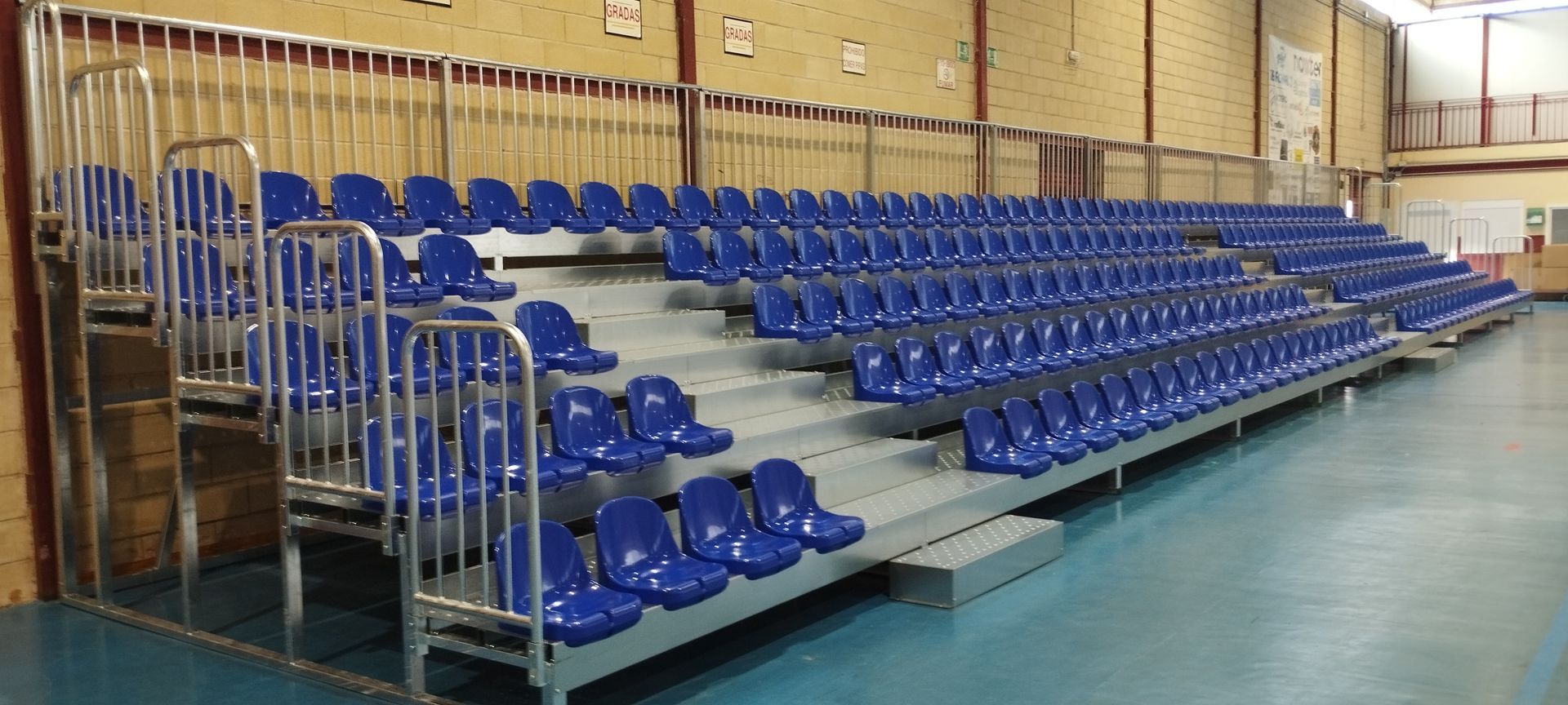 Una fila de asientos azules en un estadio con una barandilla de metal.