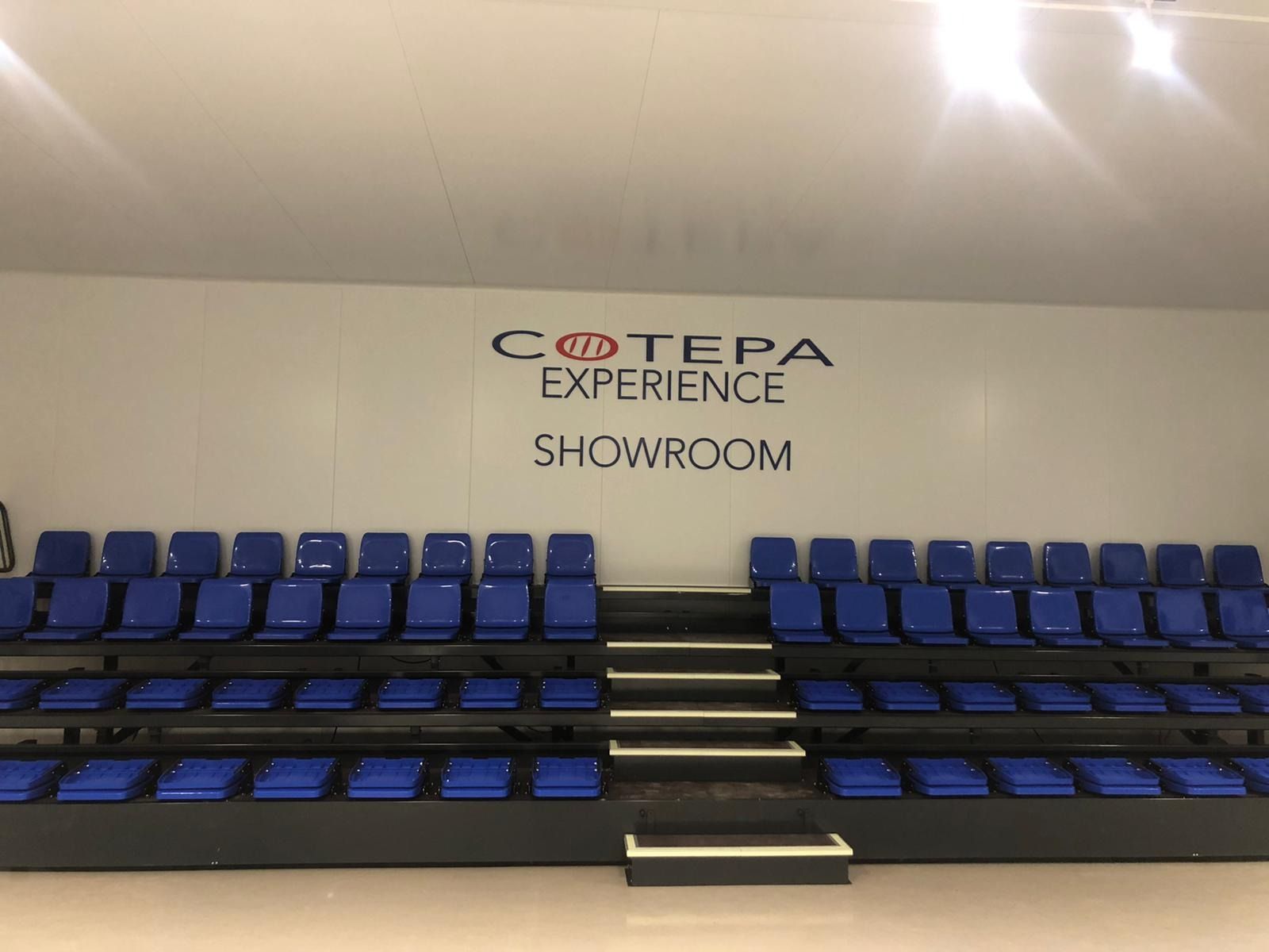 Una sala de exposición con filas de asientos azules y escaleras.