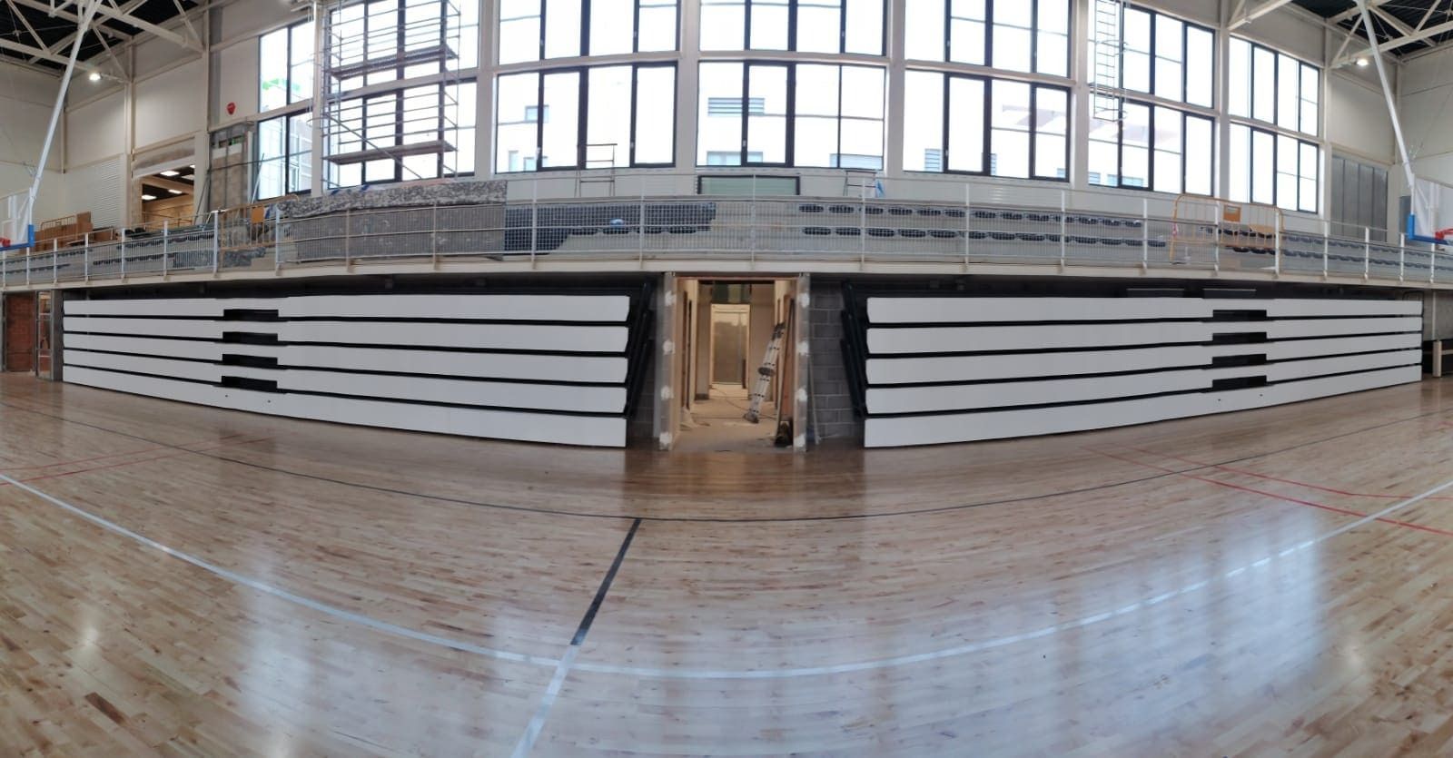 Un gran gimnasio con suelo de madera y muchas ventanas.