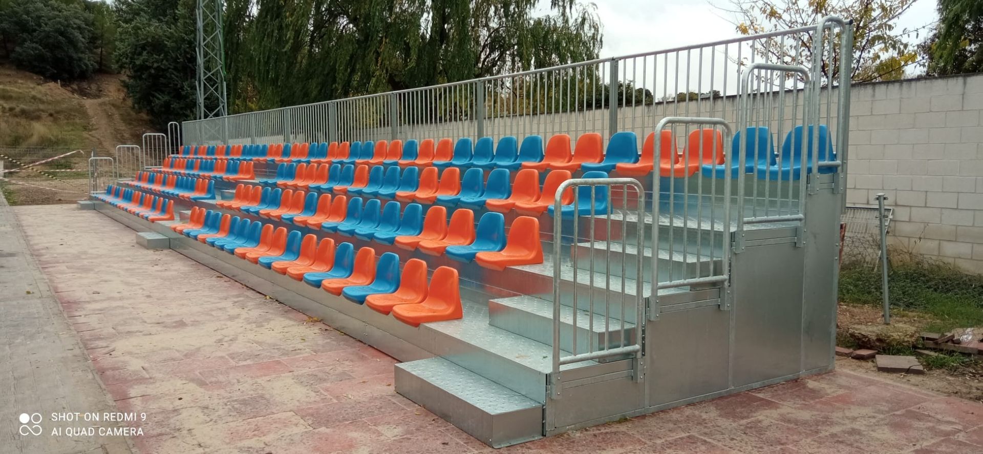 Un estadio con asientos azules y naranjas y una barandilla de metal.