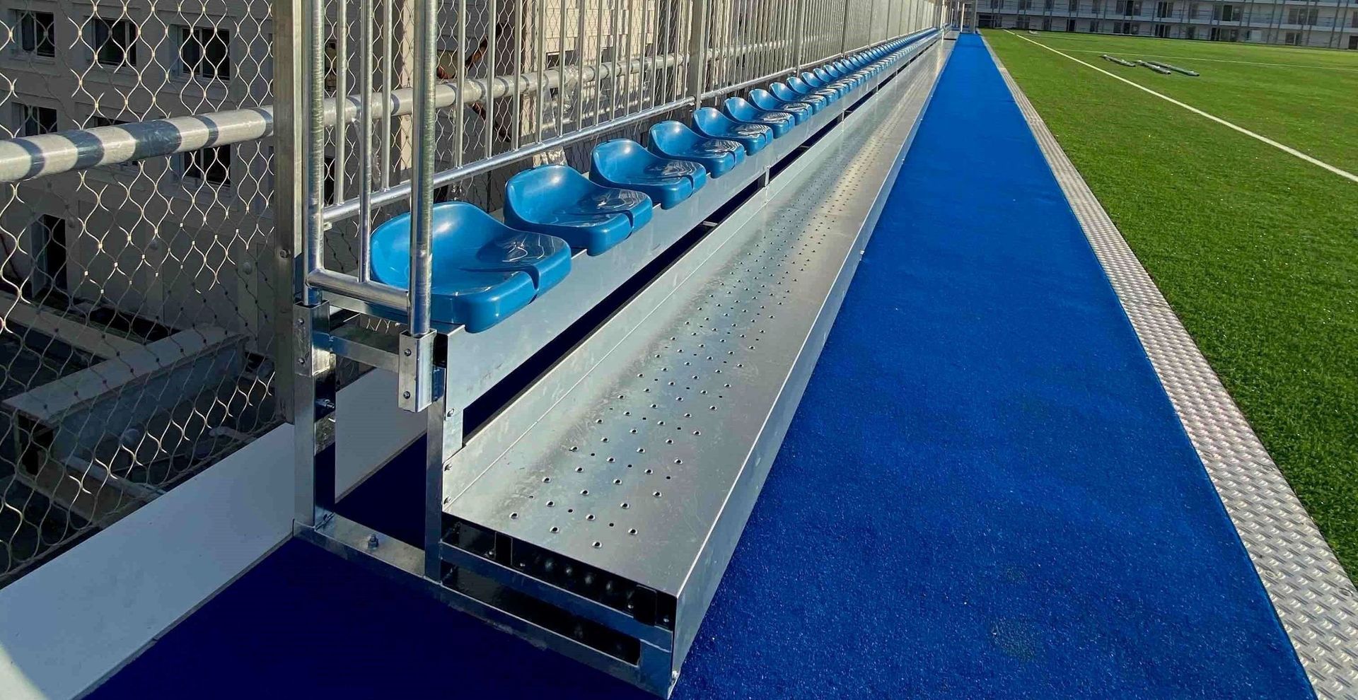 Una fila de asientos azules en un campo de fútbol al lado de una valla.