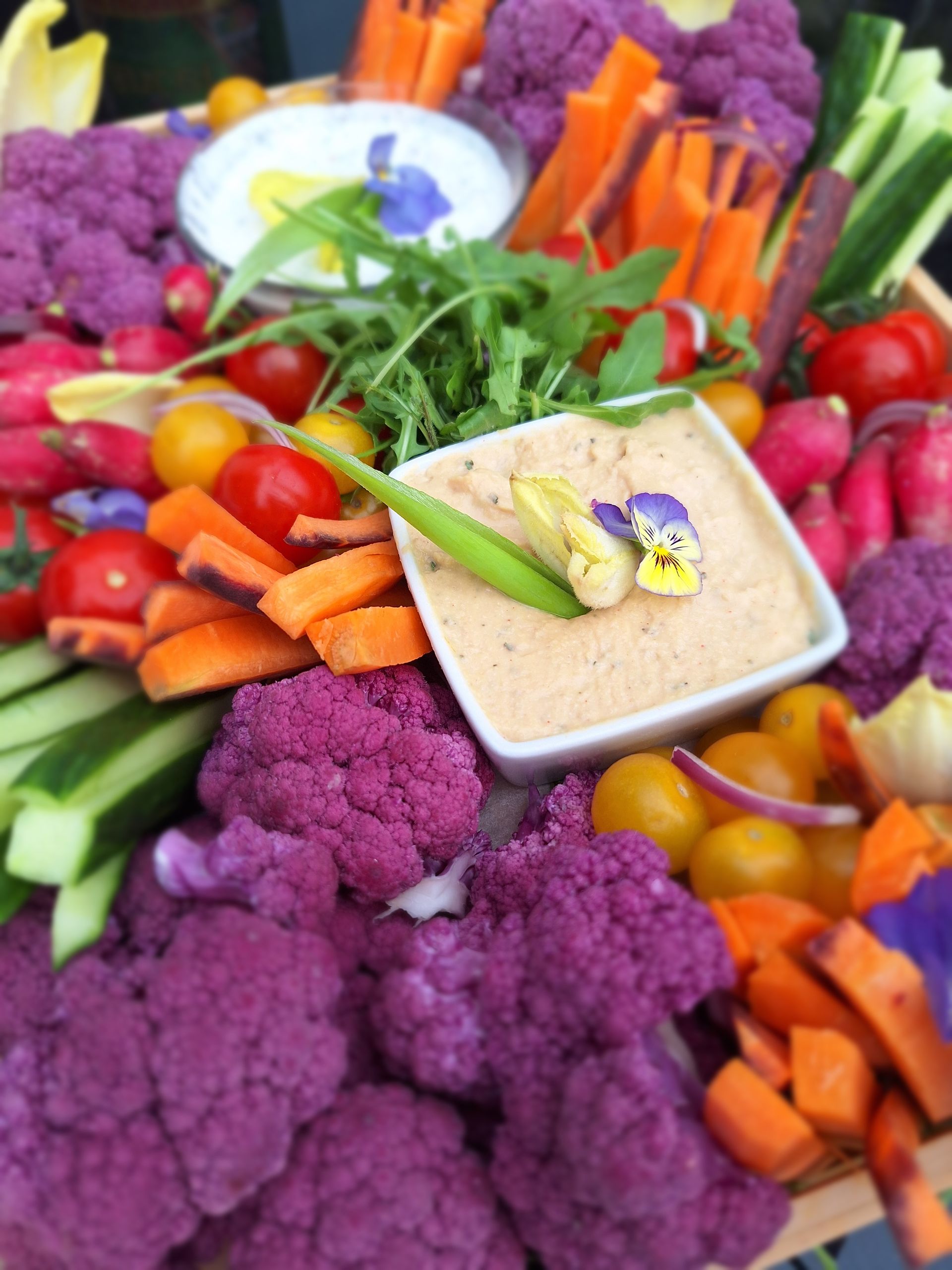 Assortiment coloré de légumes avec une sauce dip, composé de chou-fleur violet, de carottes, de concombres et de tomates cerises