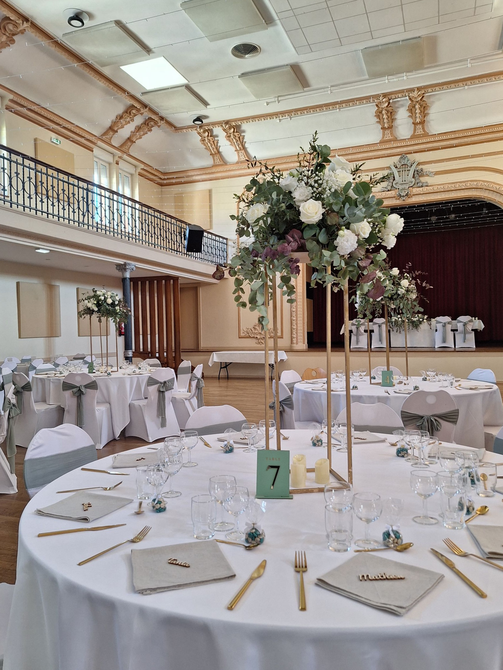 Élégante salle de réception avec des tables rondes, des nappes blanches, des touches dorées et de grands centres de table floraux