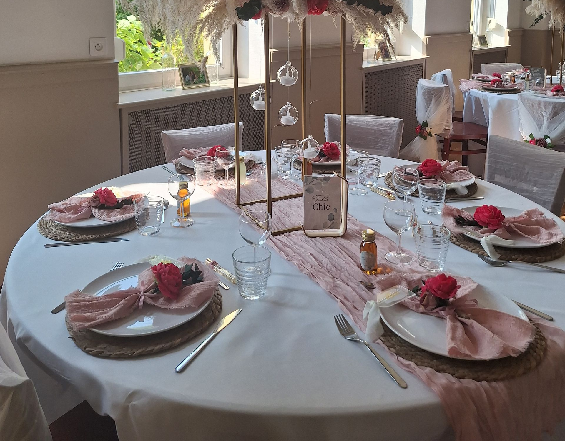 Élégant ensemble de table à manger d’extérieur avec des chaises blanches, des touches de rose, des bougies et des couverts dressés pour un repas formel