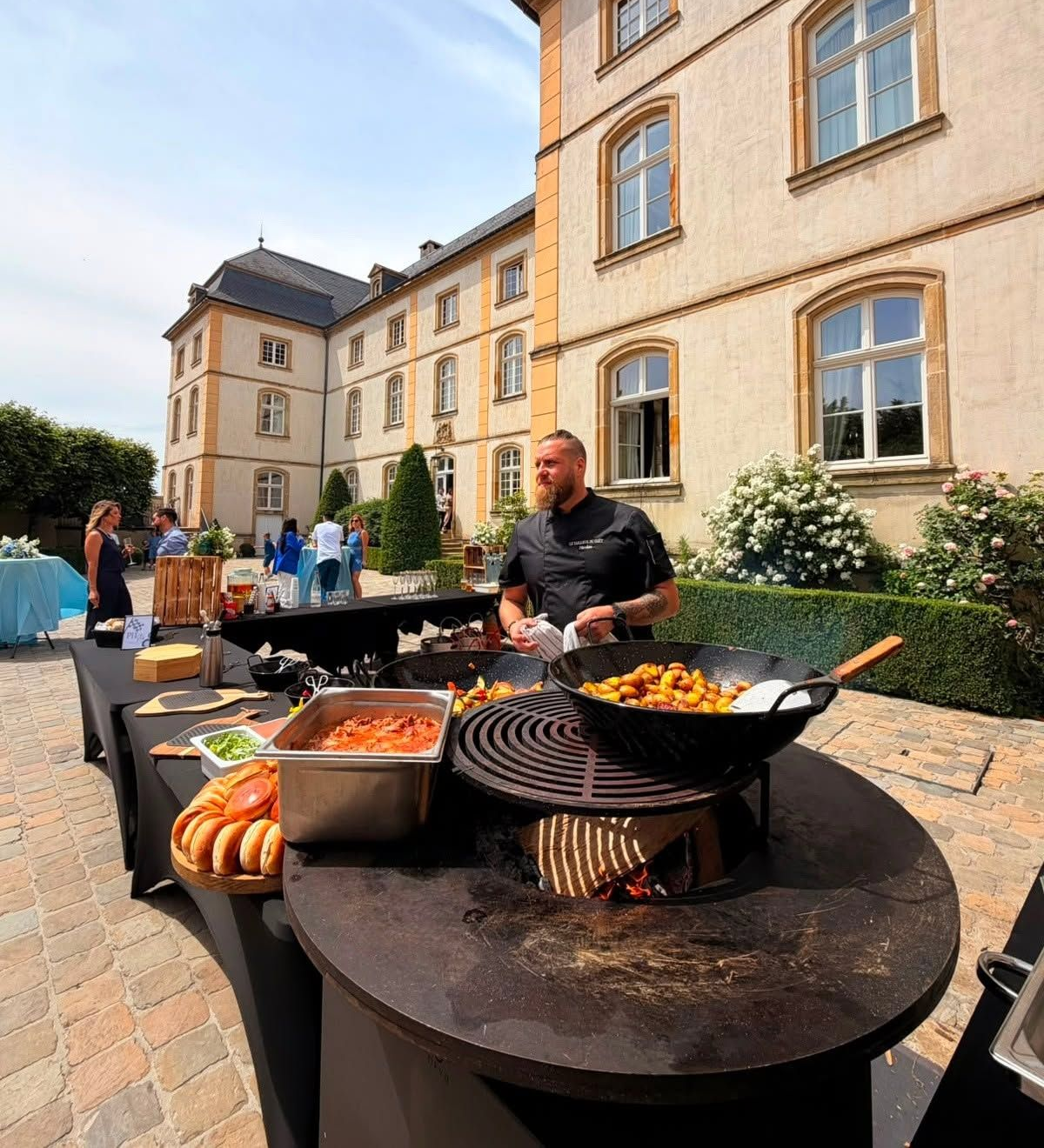 Buffet en plein air avec des grillades et un homme qui sert devant un grand bâtiment historique