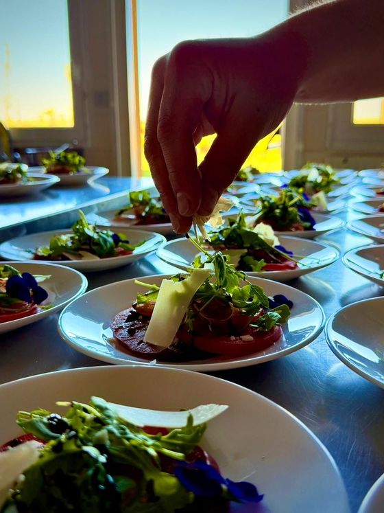 Une main dépose une garniture sur une salade dressée sur une table lumineuse près d’une fenêtre