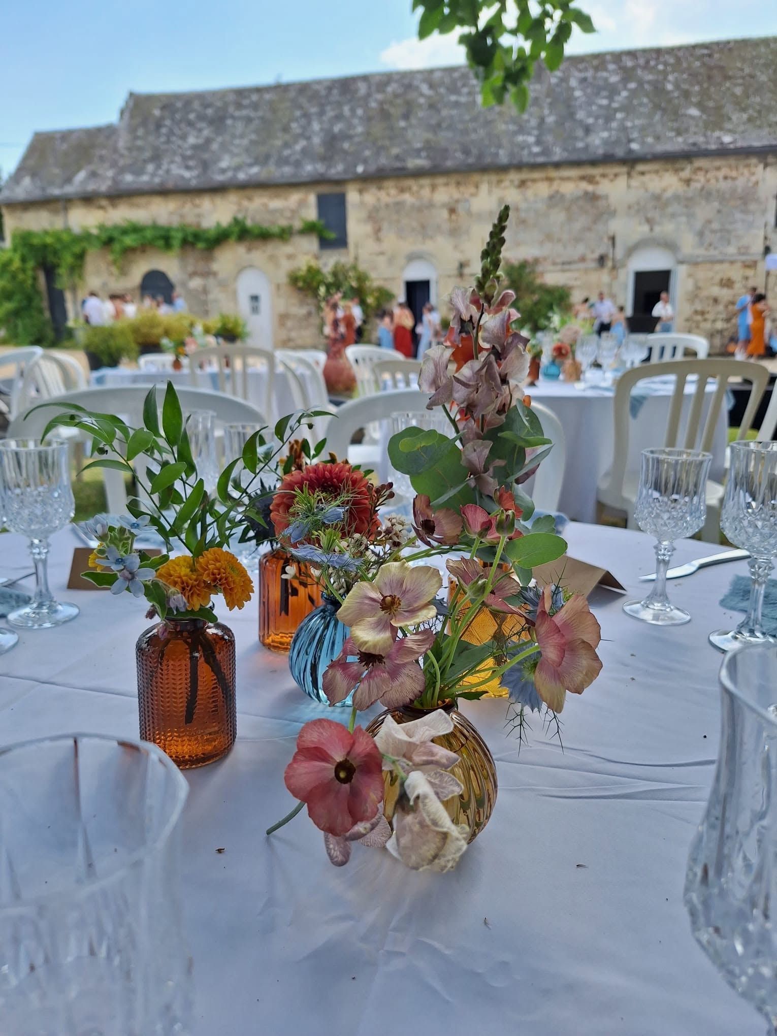 Table dressée pour un événement champêtre en plein air, ornée de fleurs, avec un bâtiment en pierre en arrière-plan