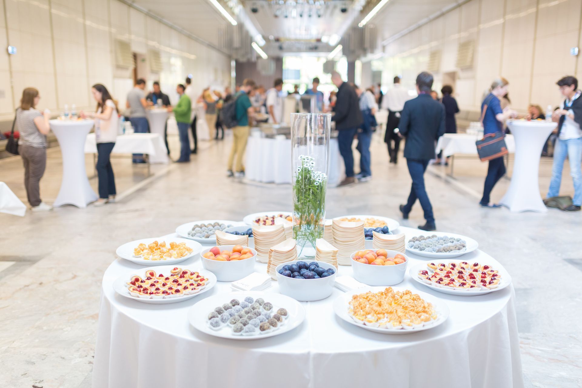 Buffet garni de hors-d’œuvre variés lors d’une réception lumineuse en intérieur, avec des invités qui discutent en arrière-plan