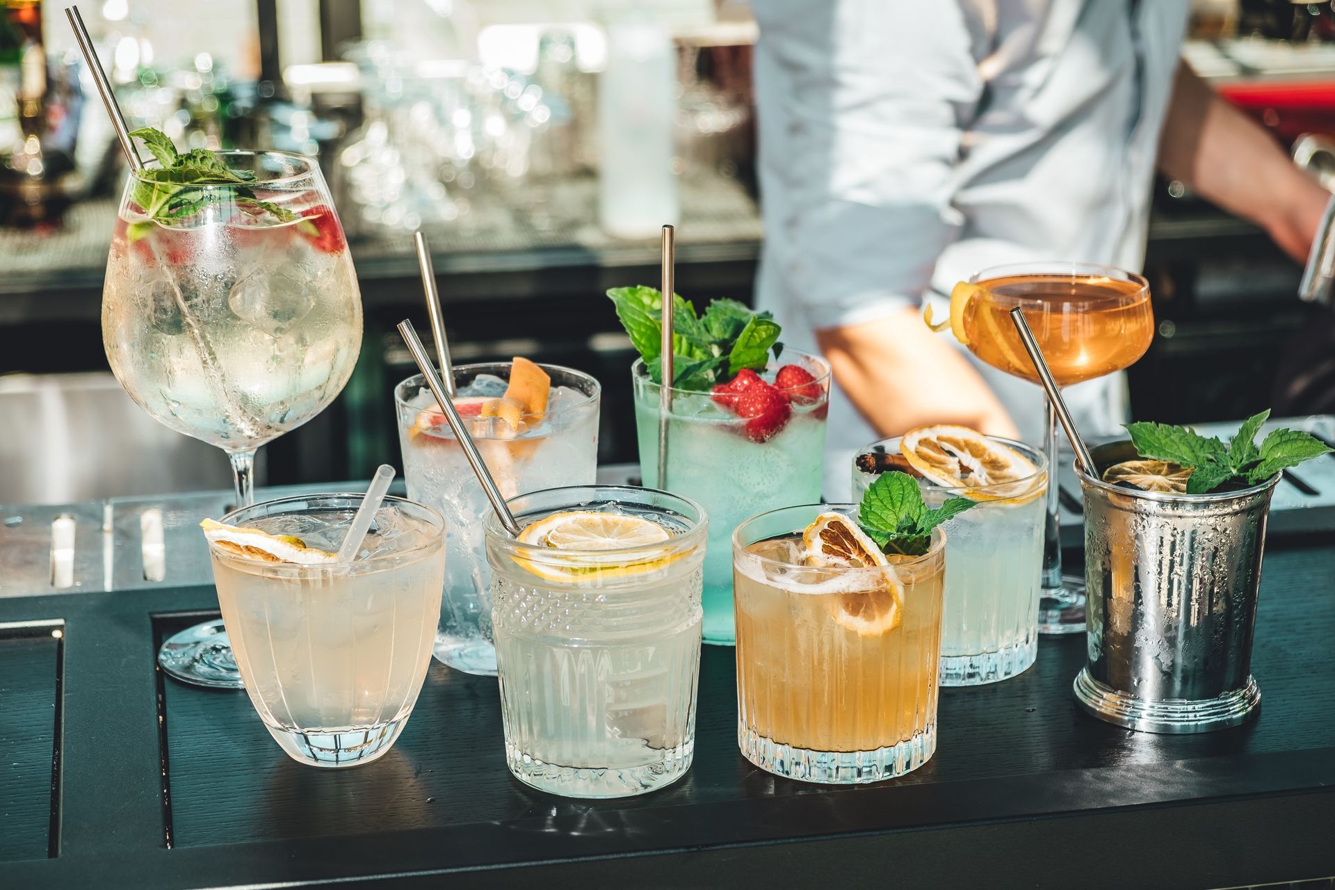 Chariot à boissons d’extérieur recouvert d’une bâche bleue, avec des bouteilles et des verres, près d’un bâtiment sur une pelouse ensoleillée