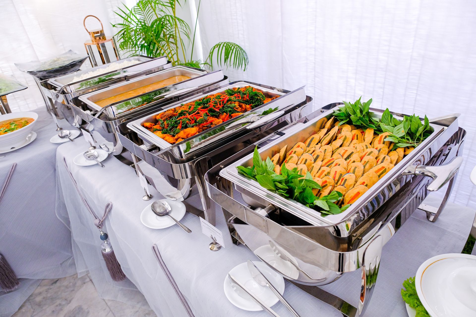 Table de buffet avec des plats de maintien au chaud en inox contenant des salades et des légumes, ainsi que des gressins, lors d’un événement avec traiteur