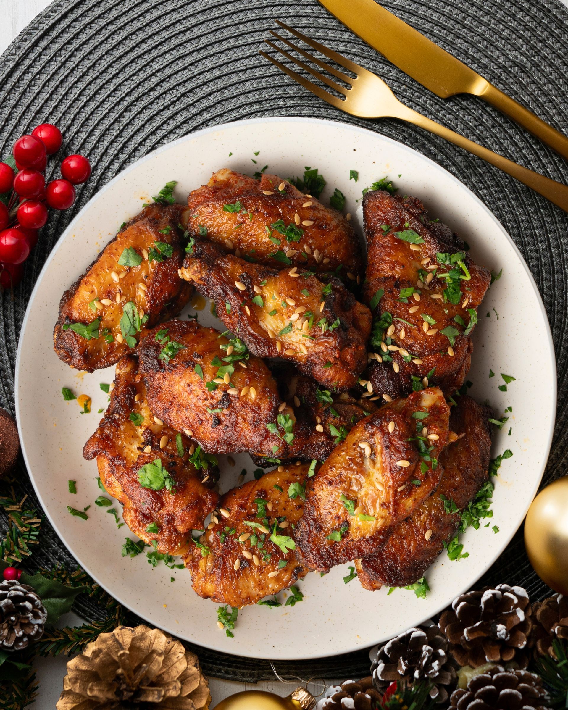 Morceaux de poulet glacés dressés dans une assiette blanche, garnis d’herbes, avec des couverts dorés et des baies rouges à proximité