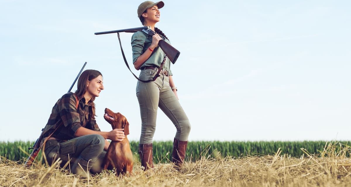 Dos mujeres están paradas en un campo con sus perros.