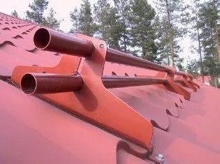 Punainen peltikatto, jossa on kaksi tuuletusputkea ja harjakatto, taustalla mäntyjä