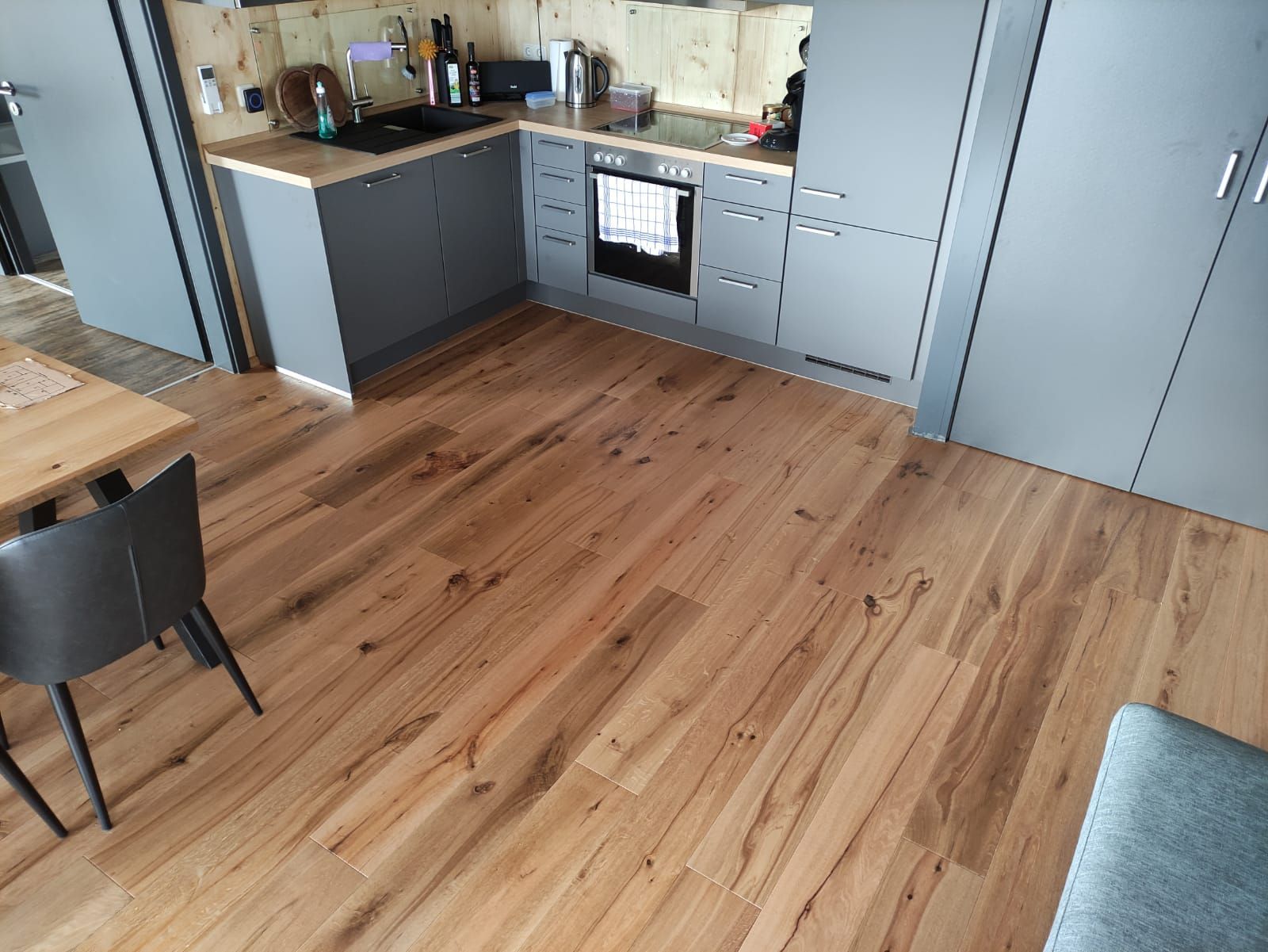 Holzboden in einer Küche mit grauen Schränken und Geräten.