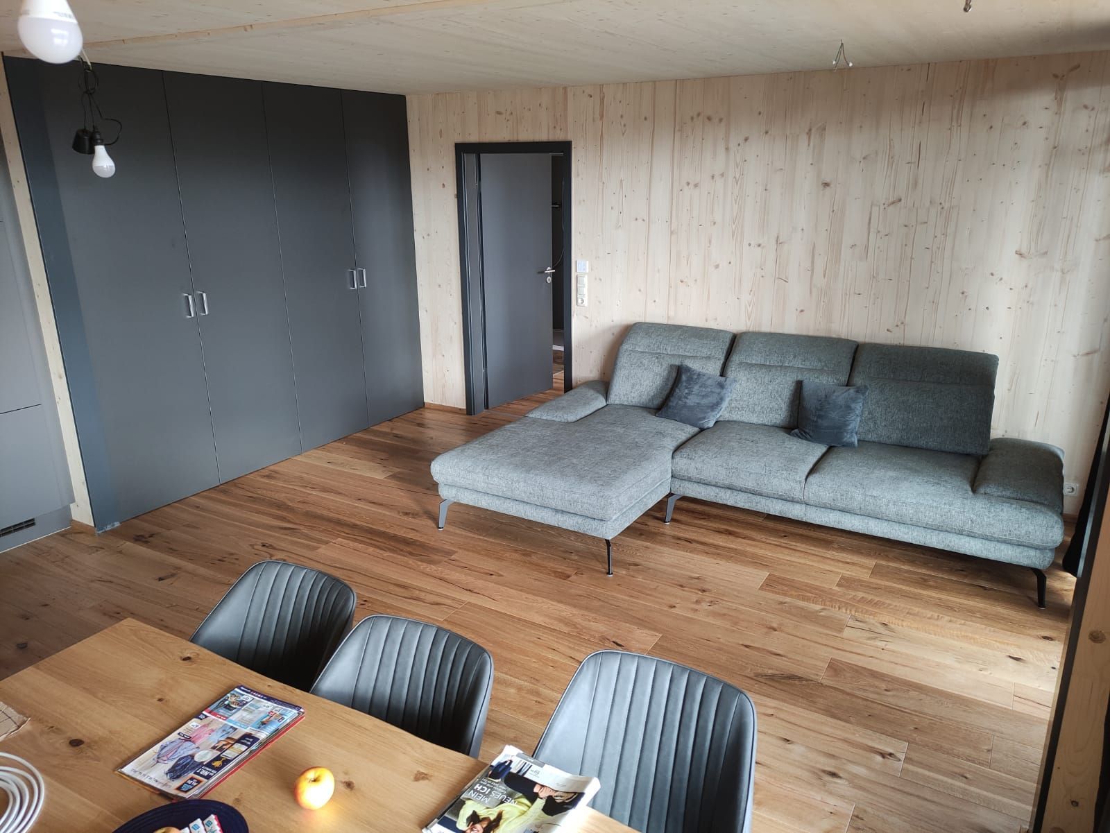 Wohnzimmer mit grauem Sofa, Holzboden, Esstisch etc.